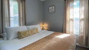 Een opgemaakt bed met een geribbelde deken, een plafondventilator en een wandlamp.