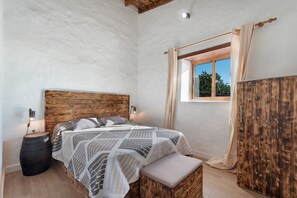 A bedroom with a wooden headboard, a bed with patterned bedding, a bedside lamp, a wooden barrel, a window with curtains, and a wooden wardrobe. - Holiday Home 'El Rincón De Yeico' with Mountain View, Private Terrace and Wi-Fi (Isora)