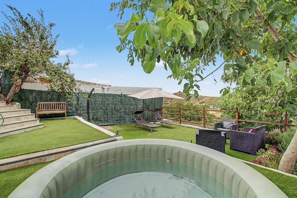 Un patio trasero con piscina, banca de madera y césped.