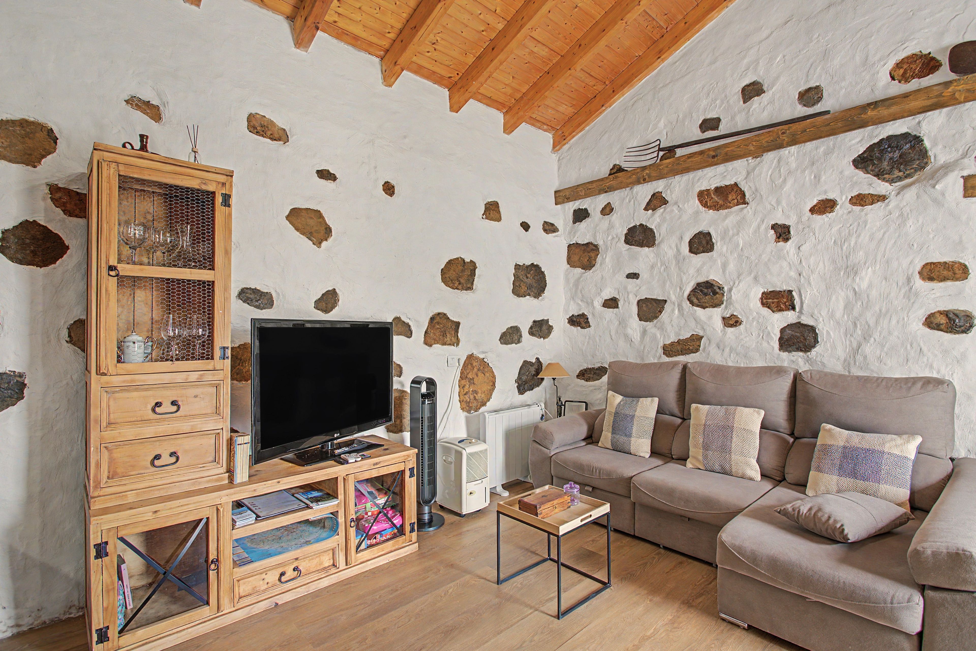 Een woonkamer met een stenen muur, houten meubels, een televisie en een bank.
