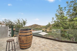 Eine Dachterrasse mit einem Holzbottich, einer Glasreling und Blick auf eine hügelige Landschaft.