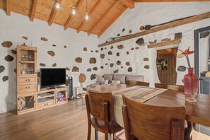Un interior rústico con una mesa de comedor de madera, sillas, un televisor y una pared de piedra.