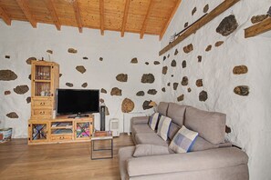 Una sala de estar con pared de piedra, muebles de madera, un televisor y un sofá.