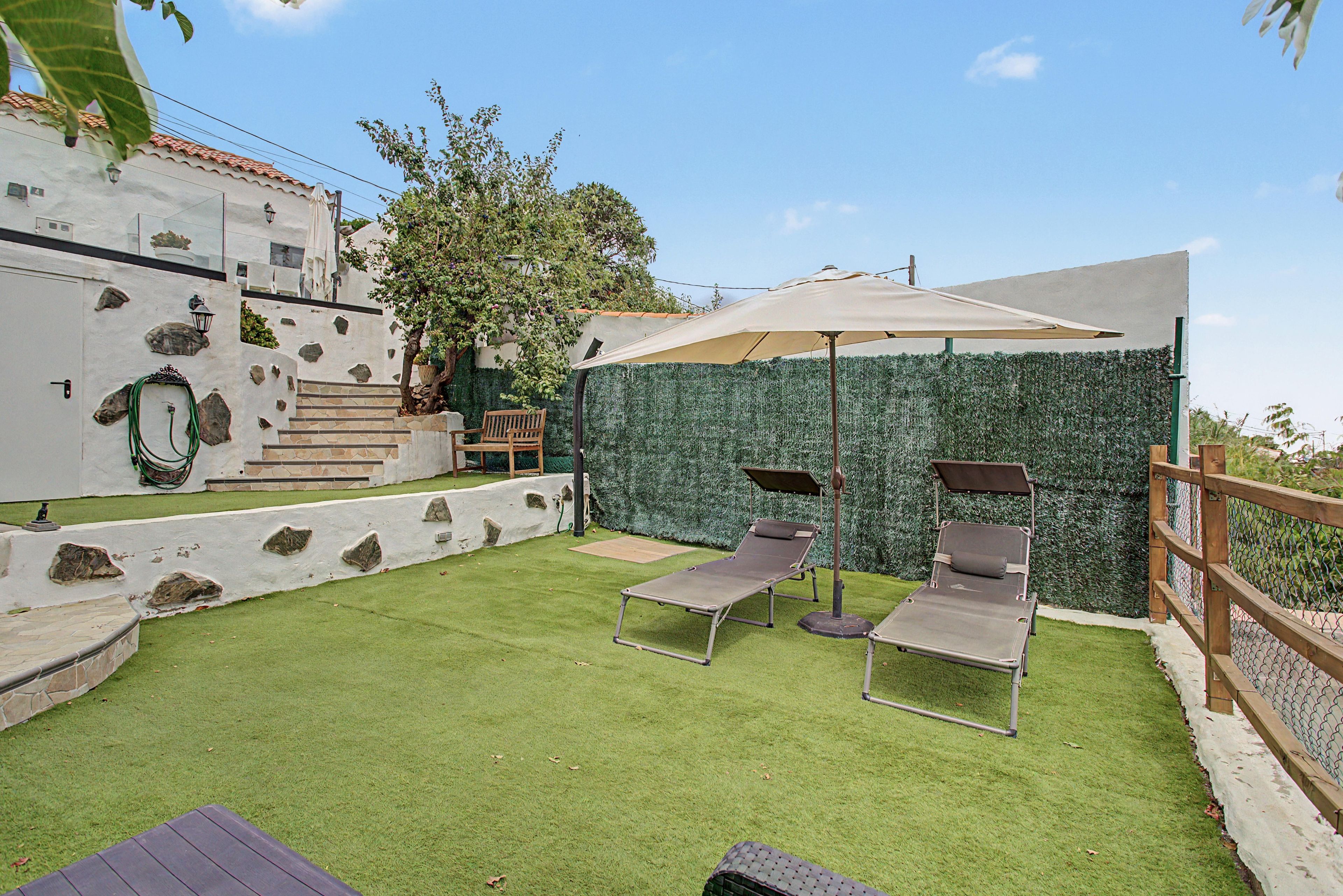 A patio with artificial grass, two lounge chairs, a wooden bench, and a decorative wall with rocks and plants.