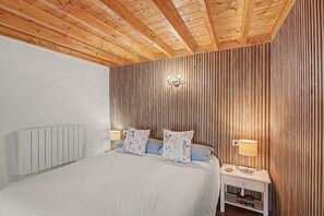 Ein Schlafzimmer mit Holzboden, einem Bett mit blumigen Kissen, einem Nachttisch mit Lampe und einer Wandleuchte.