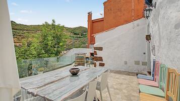 Una terraza con una mesa, sillas, un cuenco decorativo y vistas a un paisaje montañoso.
