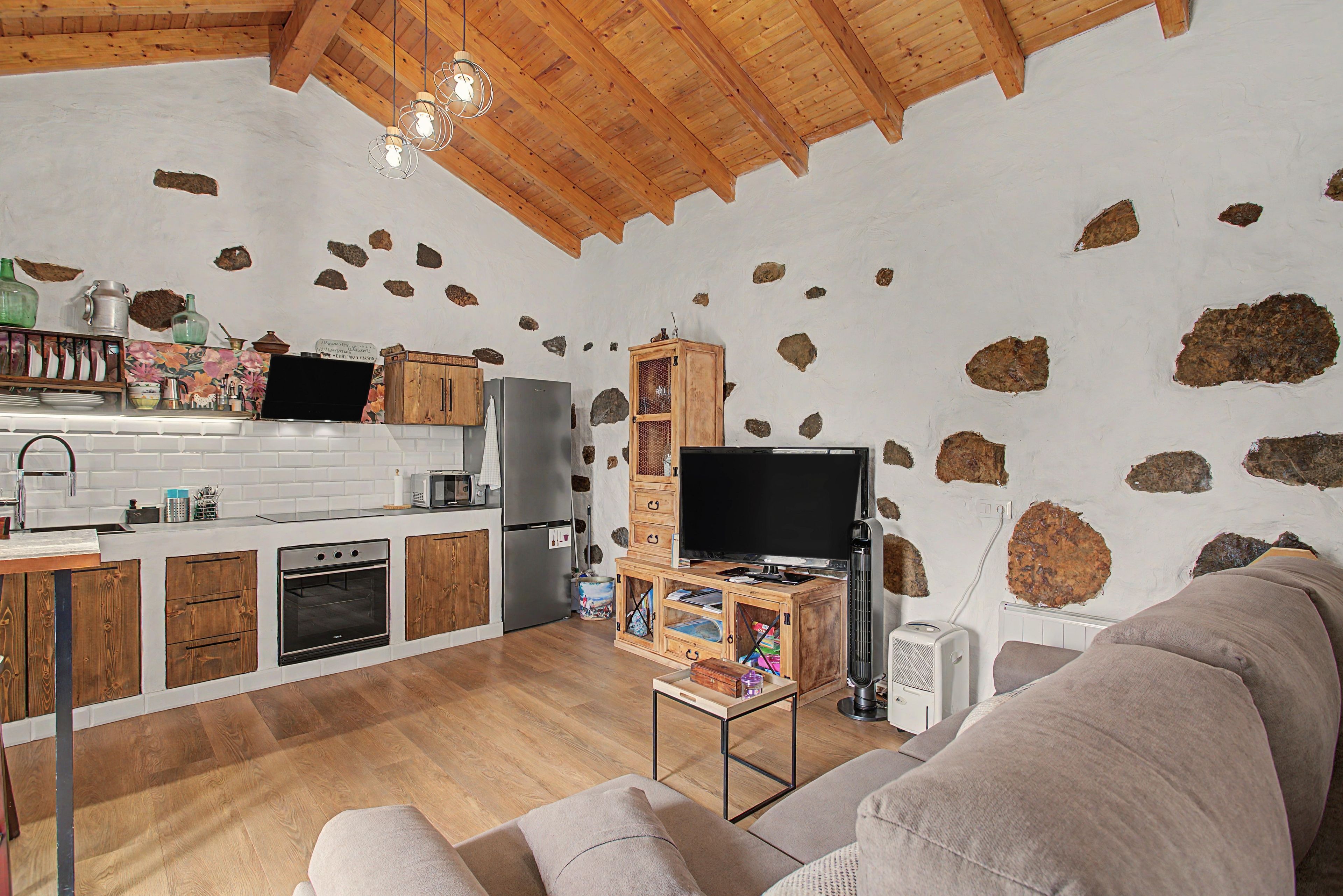 Una cocina rústica con armarios de madera, horno empotrado y pared de piedra.