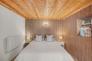 Una habitación con techo de madera, una cama con ropa blanca, dos lámparas de noche y una pared con listones de madera verticales.