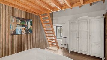 Ein Schlafzimmer mit Holzbalkendecke, einem Bild an der Wand, einer Leiter, einem Kleiderschrank und einem kleinen Tisch.