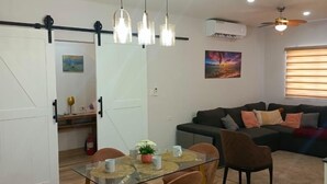 A modern living room with a glass dining table, wooden chairs, a sofa, and a ceiling fan. -  Open concept space waiting to be discovered. 
Modern accessible & affordable.  (Buccoo)