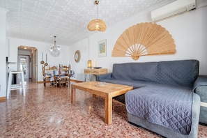 A living room with a wooden coffee table, a grey sofa, a fan, and a dining area with chairs and a table. - Holiday Apartment "Ático Cesar Cataldo" near Beach with Private Terrace (Benicarló)