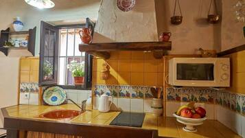 Une cuisine avec un mur recouvert de carreaux, un four à micro-ondes, un évier et une fenêtre agrémentée de plantes.