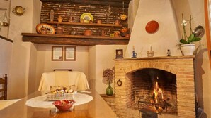 Una habitación con chimenea de ladrillo, una mesa de comedor con mantel blanco y estantes con diversos objetos.