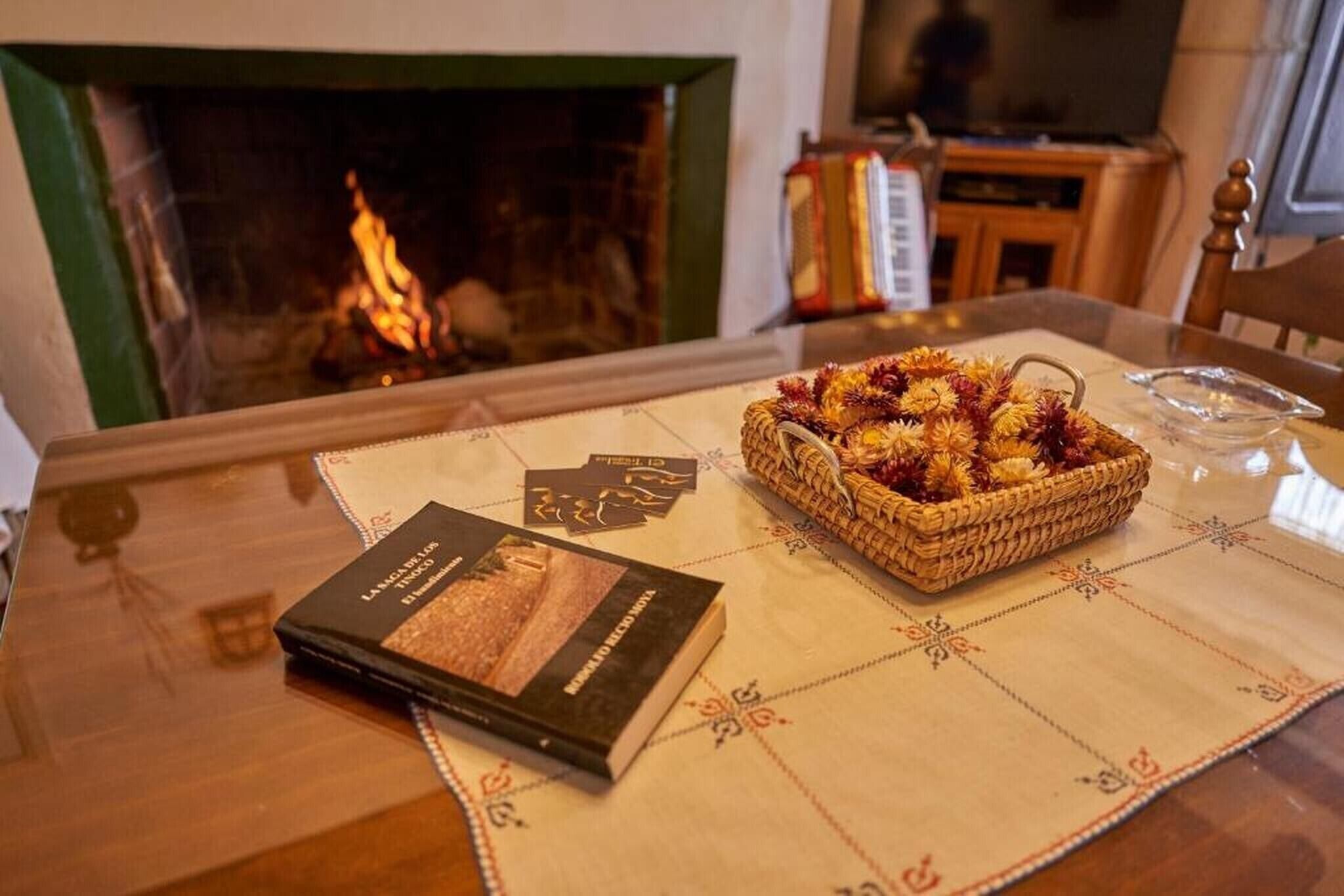 Una mesa con un libro, una cesta de flores y una chimenea al fondo.