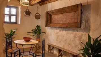 Un intérieur rustique avec un sol en pierre, des poutres en bois, une table ronde entourée de chaises et des plantes en pot.