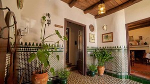 A room with a tiled floor, potted plants, a wooden ceiling, and a door leading to another room.