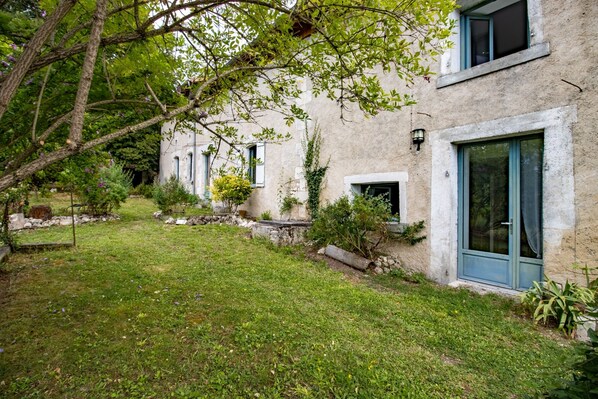 A building with a stone facade, a grassy yard, and a tree with purple flowers.