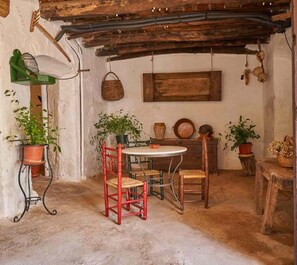 A rustic room with a wooden table, two red chairs, and potted plants.