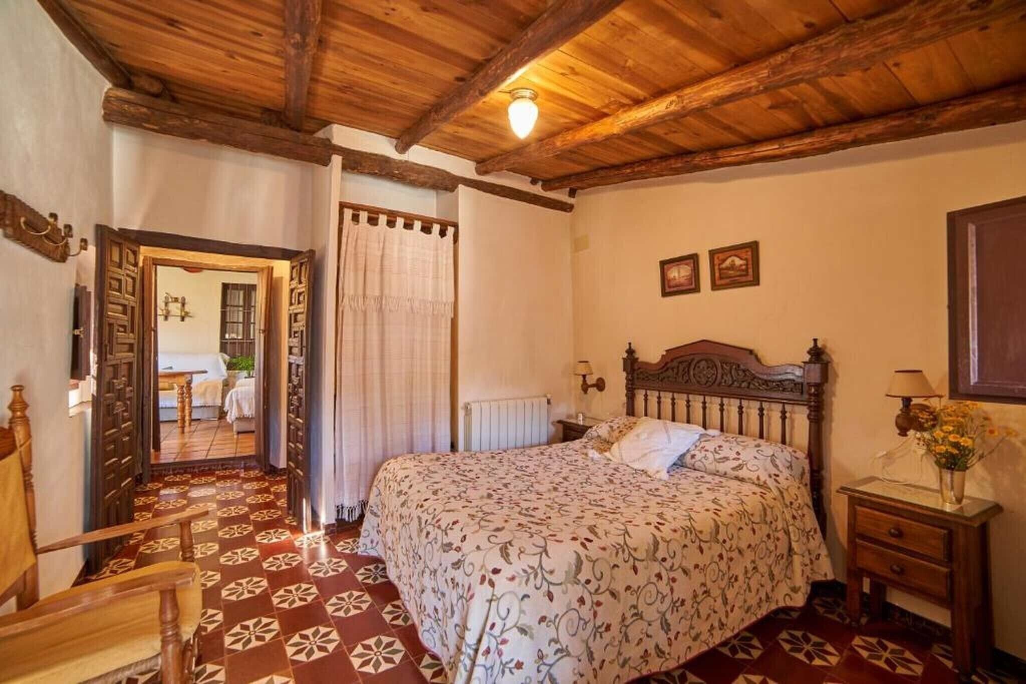 Un dormitorio con techo de madera, suelo estampado, cama con cabecera, mesita de noche y espejo.