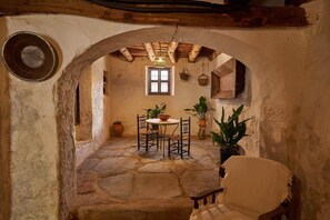 Une pièce voûtée en pierre, avec une table et des chaises, un luminaire suspendu et des plantes en pot.