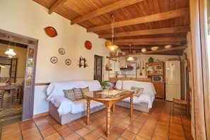 A cozy living area with a wooden ceiling, a dining table, two sofas, and a kitchen in the background. - Country House 'Tragaluz Il' with Mountain View, Shared Terrace and Wi-Fi (Fuenteheridos)