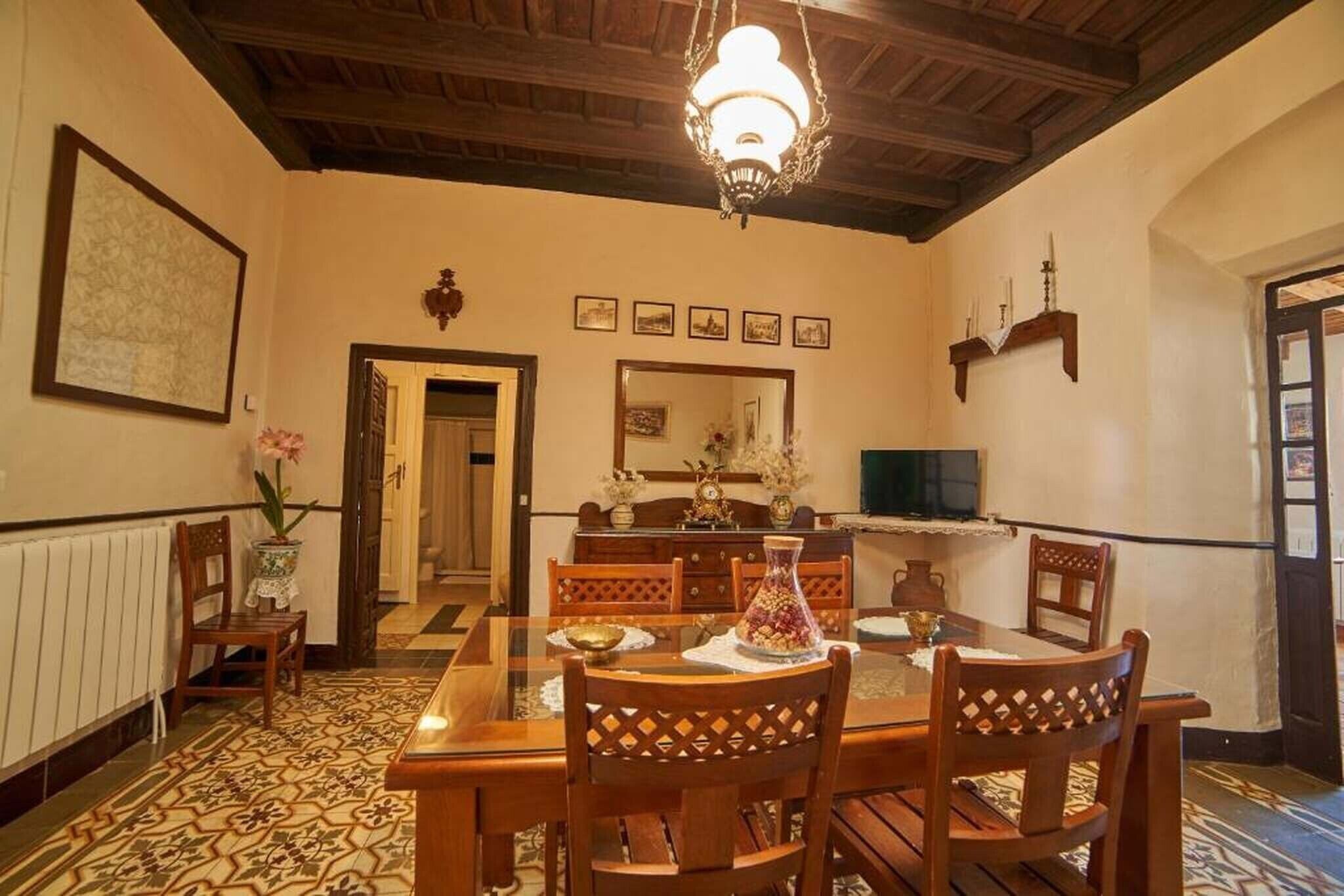 A dining area with a wooden table, chairs, a chandelier, and a tiled floor.