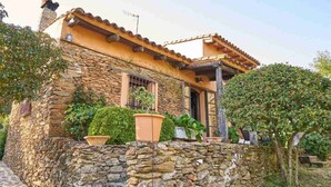 A stone building with a tiled roof, a stone wall in front, and potted plants.