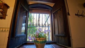 A window with a potted plant, wooden shutters, and a view of greenery outside.