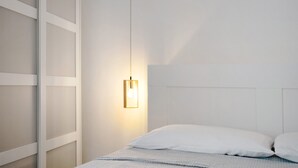 Una cama bien hecha con sábanas blancas, una lámpara colgante y una pared con un diseño geométrico.