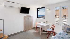Una habitación con una mesa blanca, dos sillas, un televisor, una puerta de madera y una ventana con vistas.