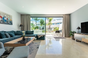 Una sala de estar moderna con sofá, mesa de centro, televisor y un balcón con mobiliario exterior.