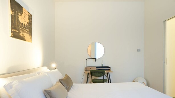 Ein Schlafzimmer mit einem Bett, einem Schreibtisch mit Stuhl, einem runden Spiegel und einem Wandbild.