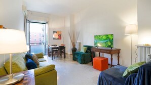 A modern living room with a sofa, a small table, a TV, and a dining area.