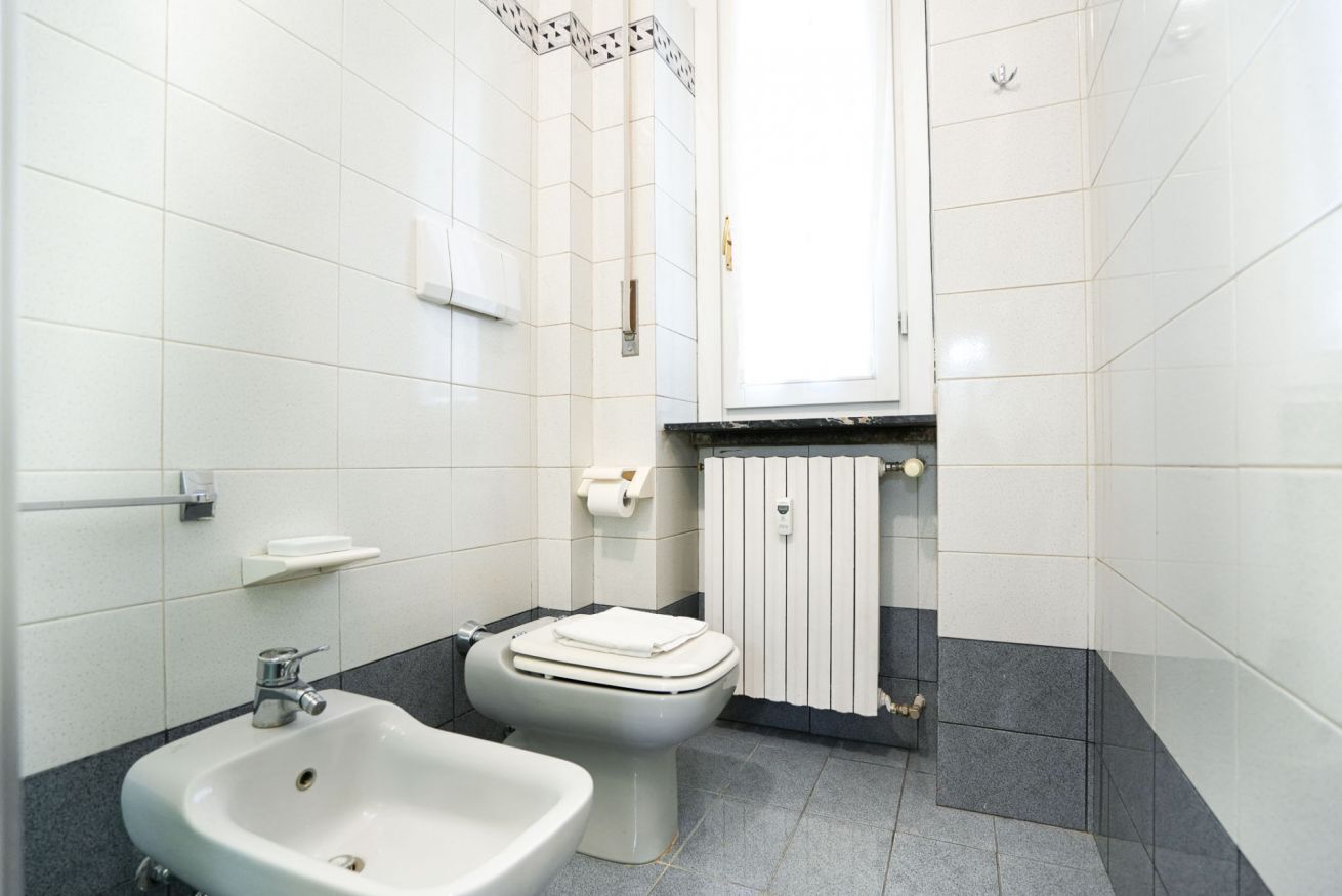 A bathroom with white tiles, a sink, a toilet, and a towel rack.