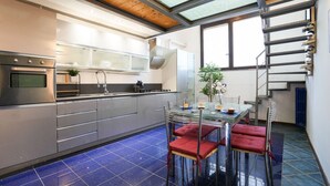 A modern kitchen with a glass dining table, red cushioned chairs, and a blue-tiled floor. - Milano, Industrial Loft (Milano)