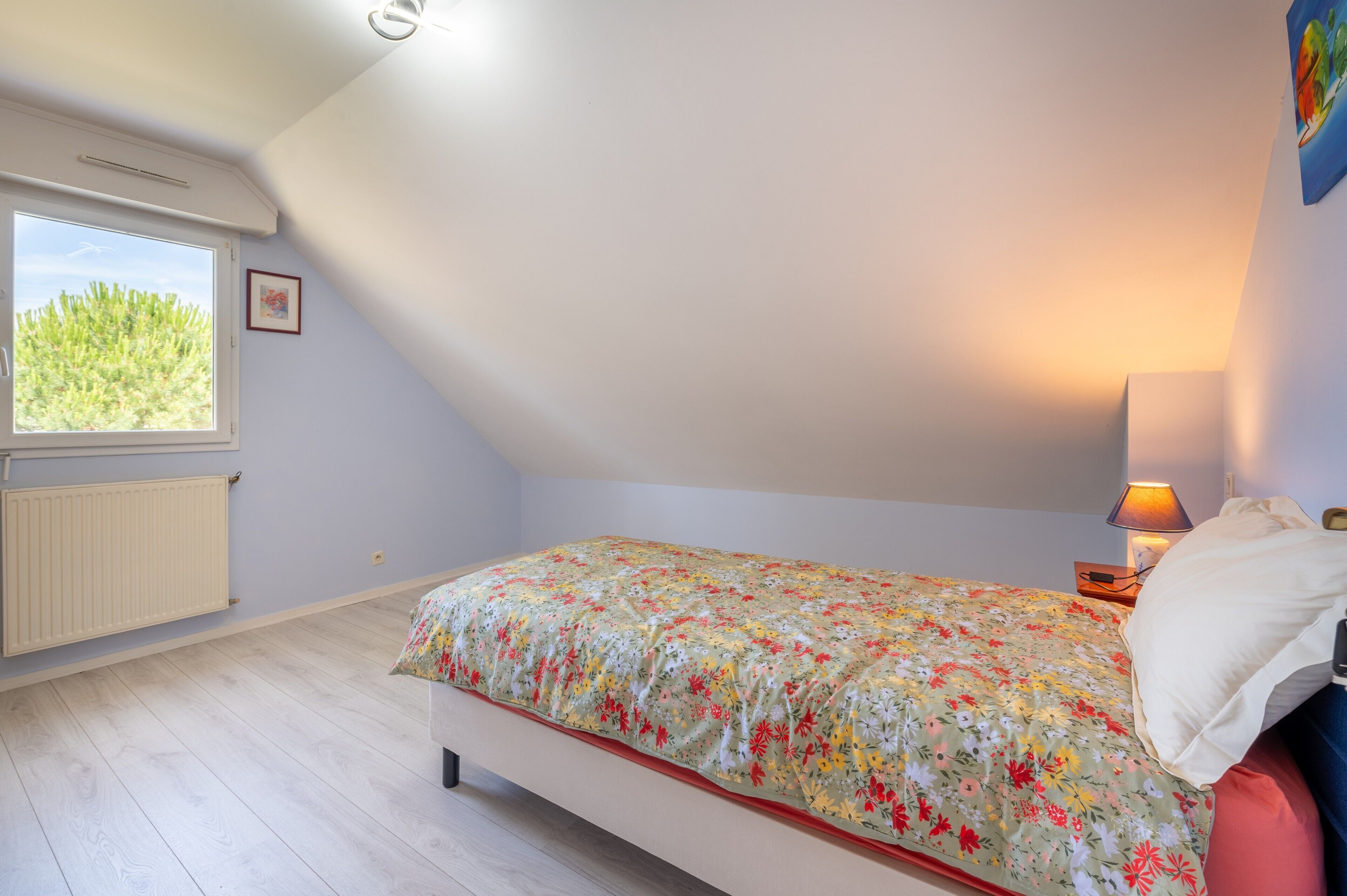 A bedroom with a bed, a window, a radiator, and a lamp.