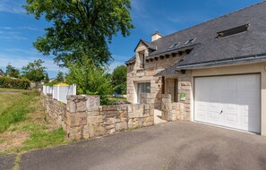 A stone house with a garage, a stone wall, and a grassy area.
