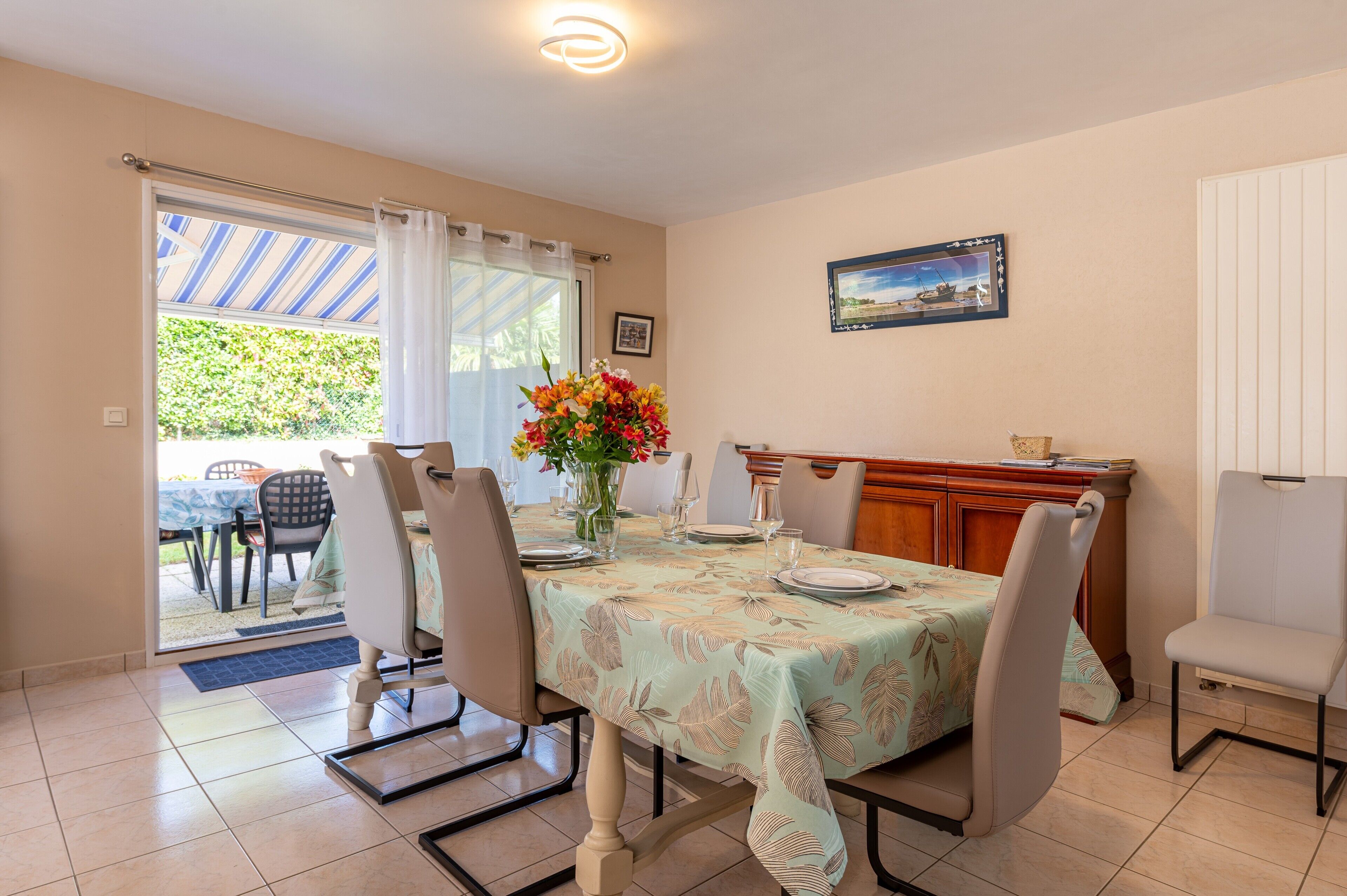 A dining area with a table set for four, chairs, a vase with flowers, and a view through a glass door to the outside.