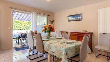 A dining area with a table set for four, chairs, a vase with flowers, and a view through a glass door to the outside.