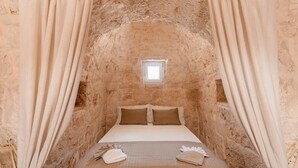 Une pièce étroite aux murs de pierre, avec un lit, des rideaux et une petite fenêtre.