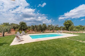 A rectangular swimming pool with a tiled deck, surrounded by a well-maintained lawn and trees.