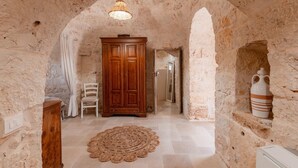 Une pièce aux murs de pierre, avec une armoire en bois, une chaise, un tapis tissé et un luminaire suspendu.