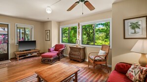 Un salon spacieux avec une table en bois, un canapé rouge, des fauteuils en osier et un ventilateur de plafond.