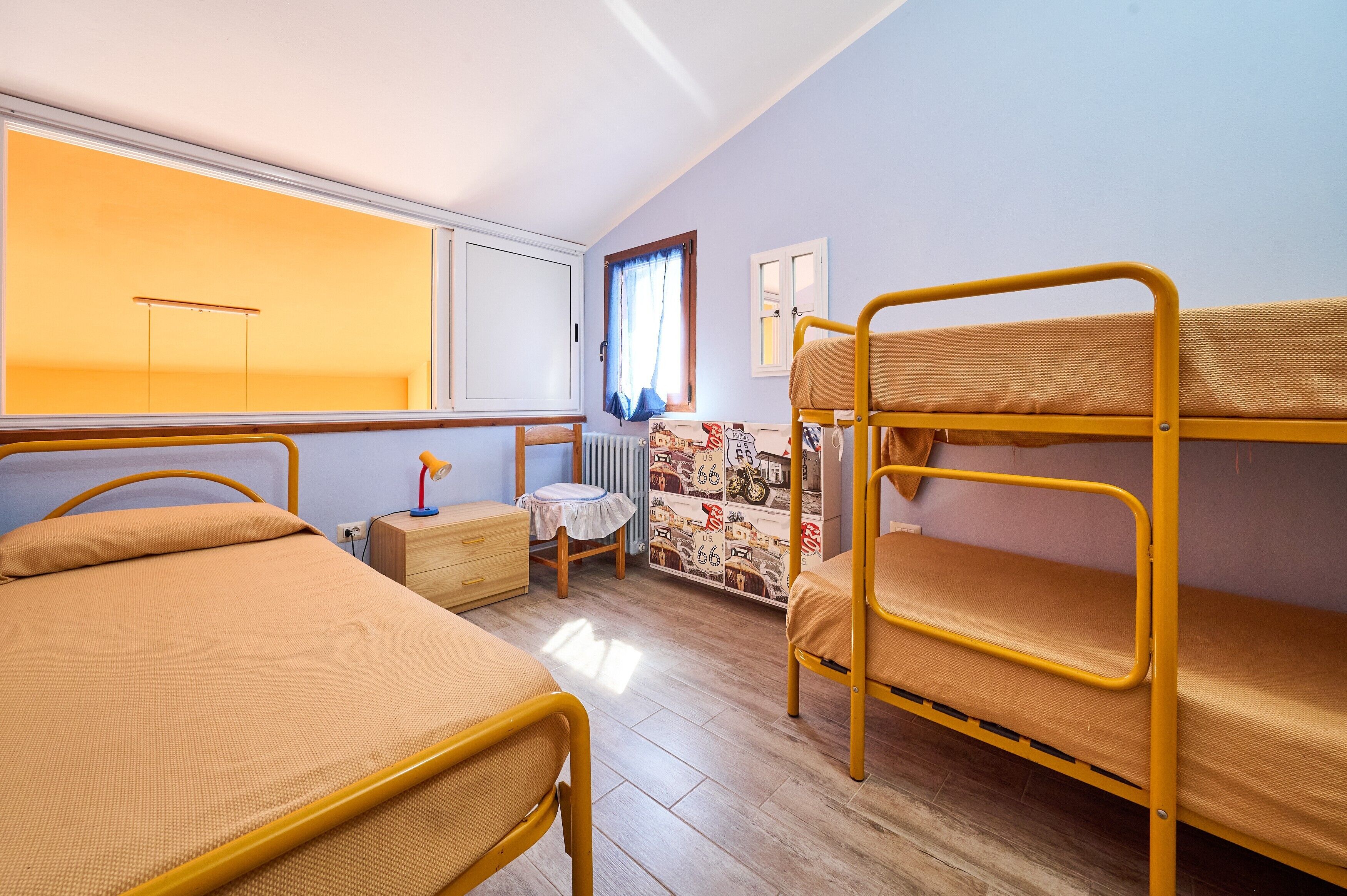 Ein Zimmer mit Etagenbetten, einem kleinen Tisch mit Lampe, einem Heizkörper und einem Fenster mit Vorhängen.