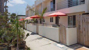 Een hotel met terras, rode parasols, een zwembad en een houten omheining.
