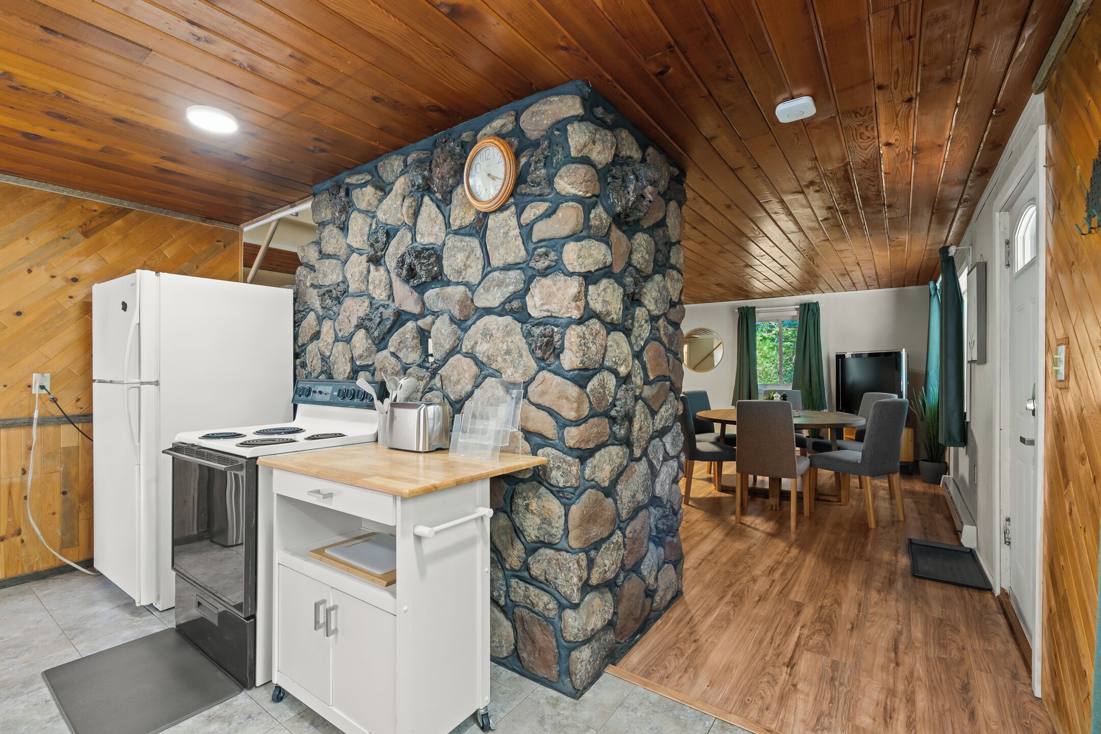 Eine Küche mit Steinwand, Holzbalkendecke und einem Essbereich mit Stühlen und Tisch.