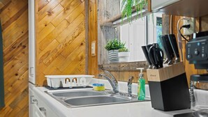 Eine Küche mit Holzboden im Fischgrätmuster, einer weißen Arbeitsplatte, einer Spüle mit zwei Becken und einem Fenster mit Pflanzen.
