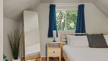 A bedroom with a bed, a bedside table with a lamp, a mirror, and a window with curtains.