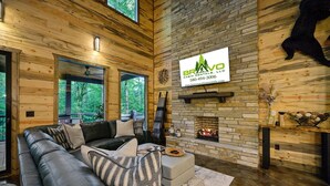 A cabin interior with a stone fireplace, a black leather sofa, and a mounted sign for Bravo Rentals, LLC. - Runaway Streams - Game Room, Mini Golf, Creekside, EV Outlet (Broken Bow)