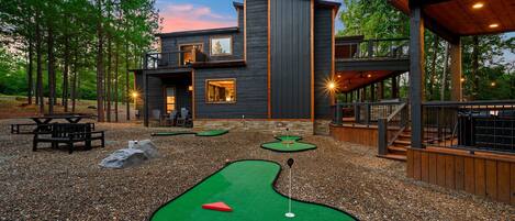 A modern house with a deck, a pool table, and a mini-golf setup.